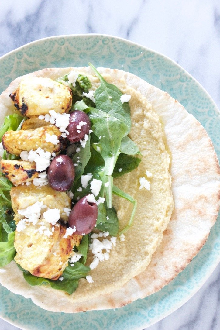 Chicken kebab on a bed of greens and hummus on a pita with feta cheese and kalamata olives