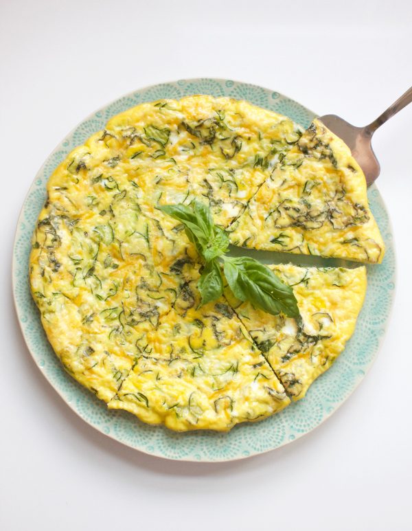 Frittata on w blue plate with a silver serving spatula and basil garnish