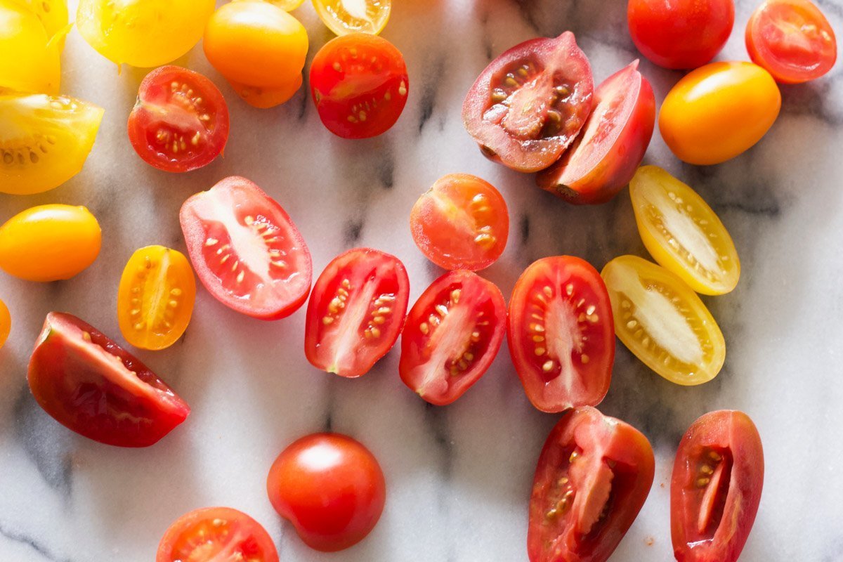 Halved grape tomatoes on a marble counter.