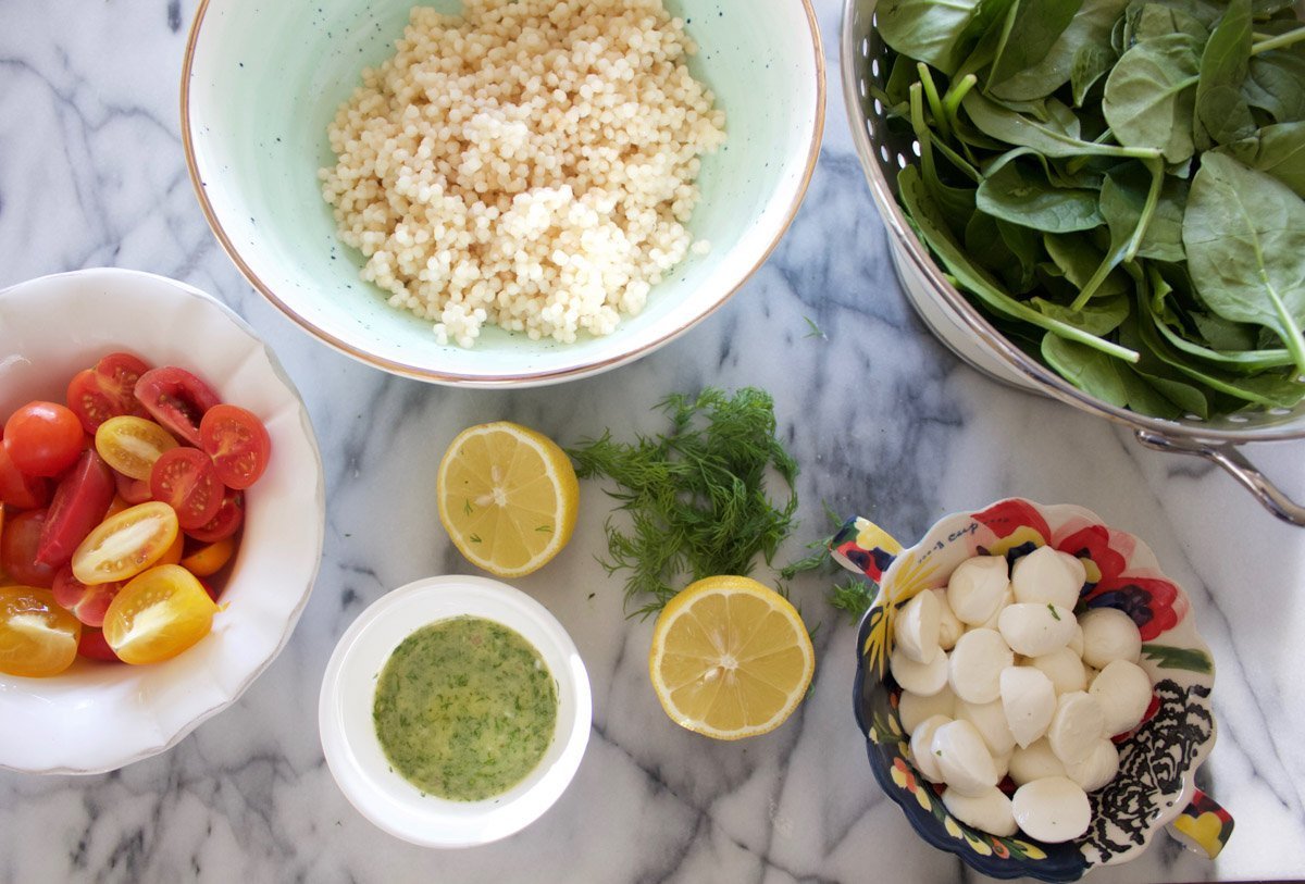 Chicken, Israeli Couscous, Spinach, Tomatoes, Fresh Mozzarella and Dill Vinaigrette in small bowls on a marble counter. 