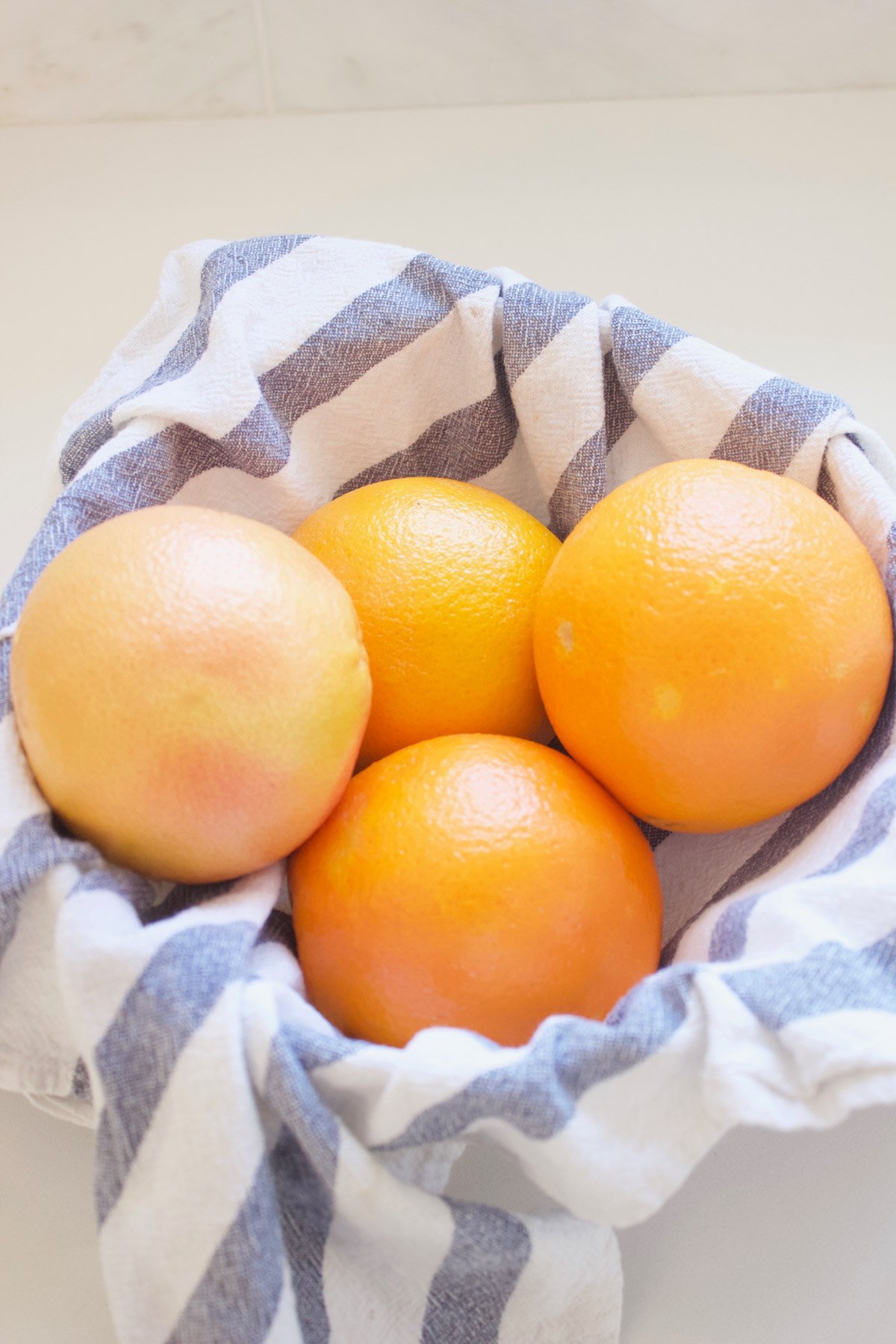 Grapefruit and oranges in a bowl with a blue and white striped wash cloth in it.