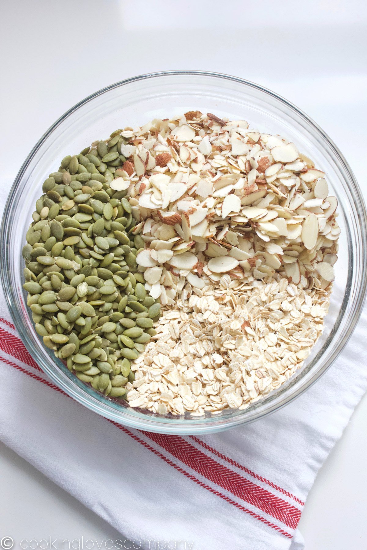 Pumpkin seeds, rolled oats and slivered almonds in a glass bowl on a counter