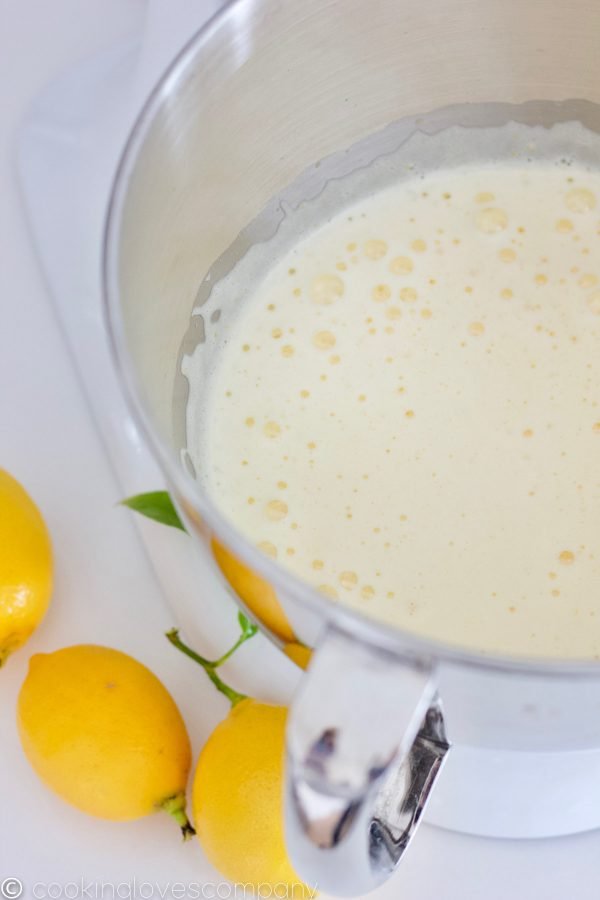 Beaten sugar and eggs in the bowl of a kitchen aid mixer with lemons on the side
