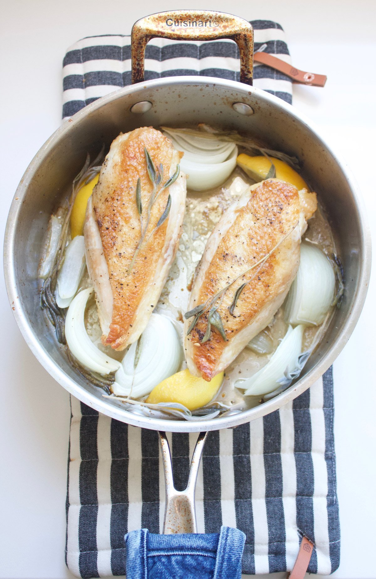 Cooked chicken breast in a pan with onions, lemon and sage.