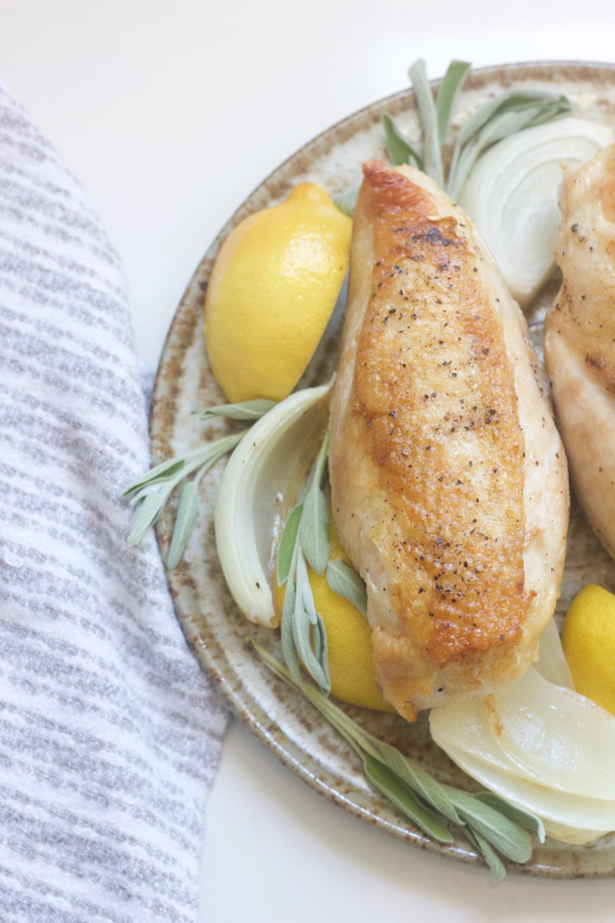 Roasted chicken on a platter with onions, lemon and sage.