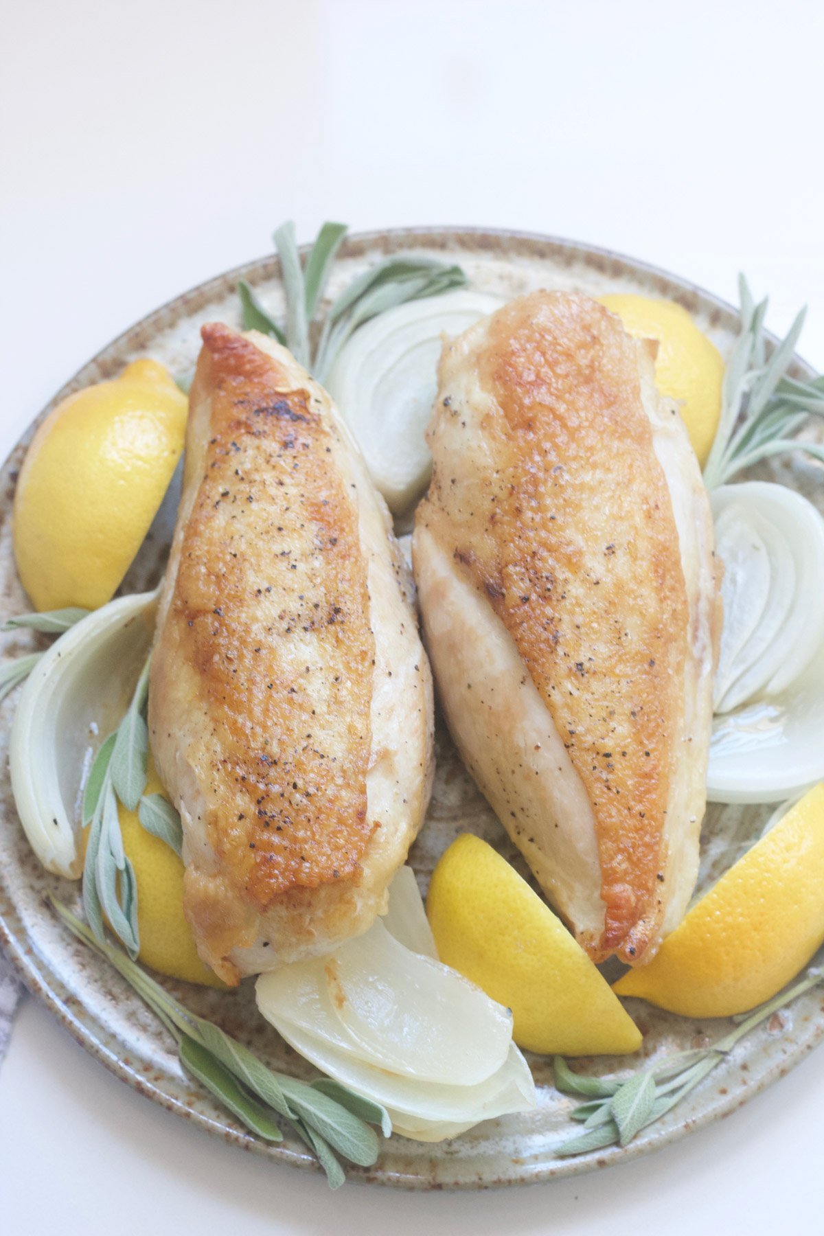 Roasted chicken on a platter with onions, lemons and sage