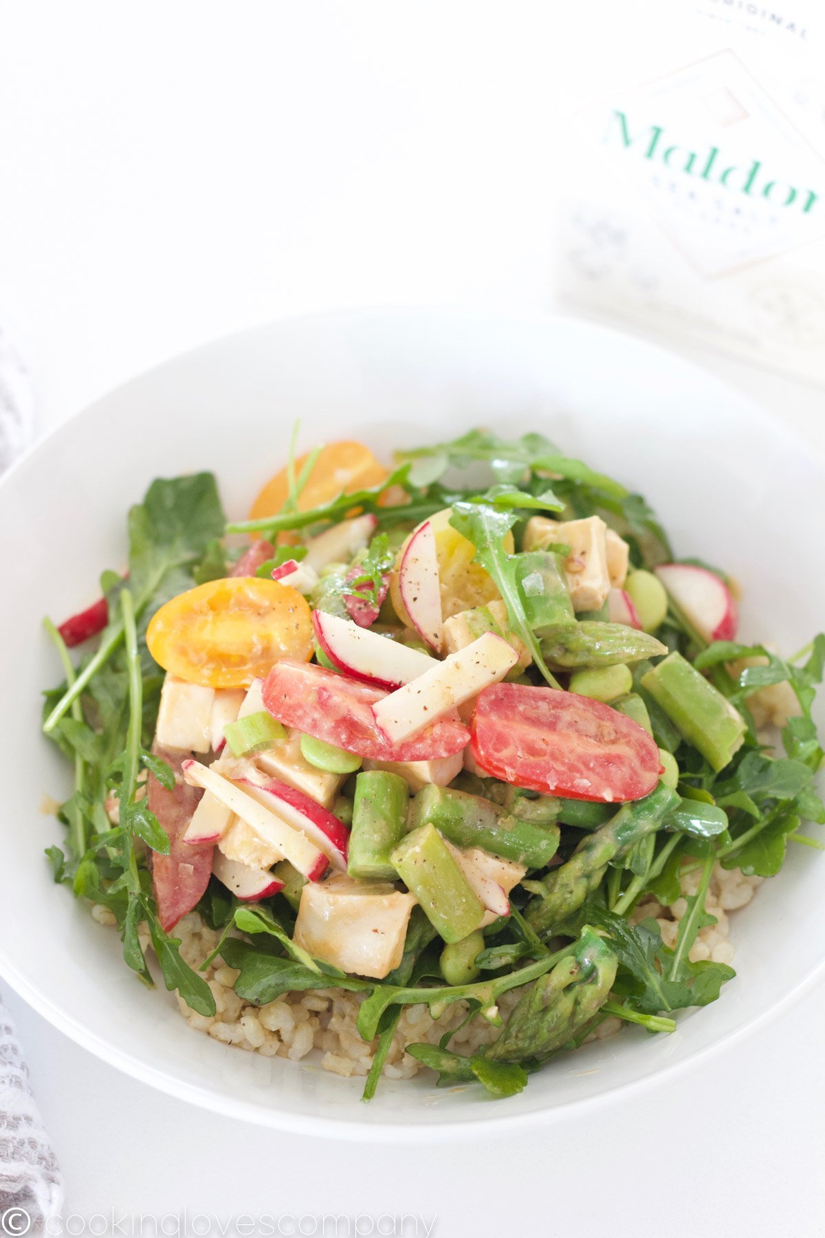 Sesame chicken rice bowl with grape tomatoes, asparagus, edamame, radishes and arugula on a towel with chopsticks