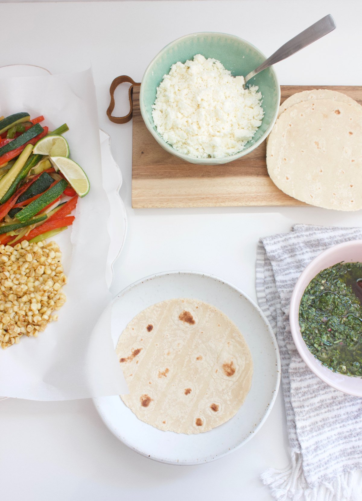 Grilled vegetables, cheese, corn tortillas and chimichurri sauce on a counter. 