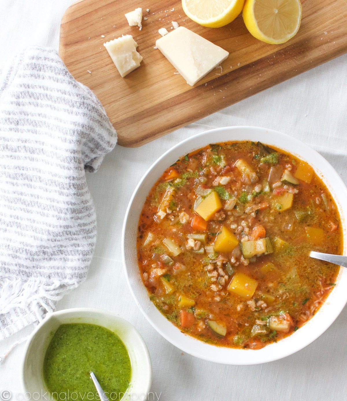 A bowl of vegetable soup with fresh pesto on a table with a bowl of pesto sauce in a small bowl on the side