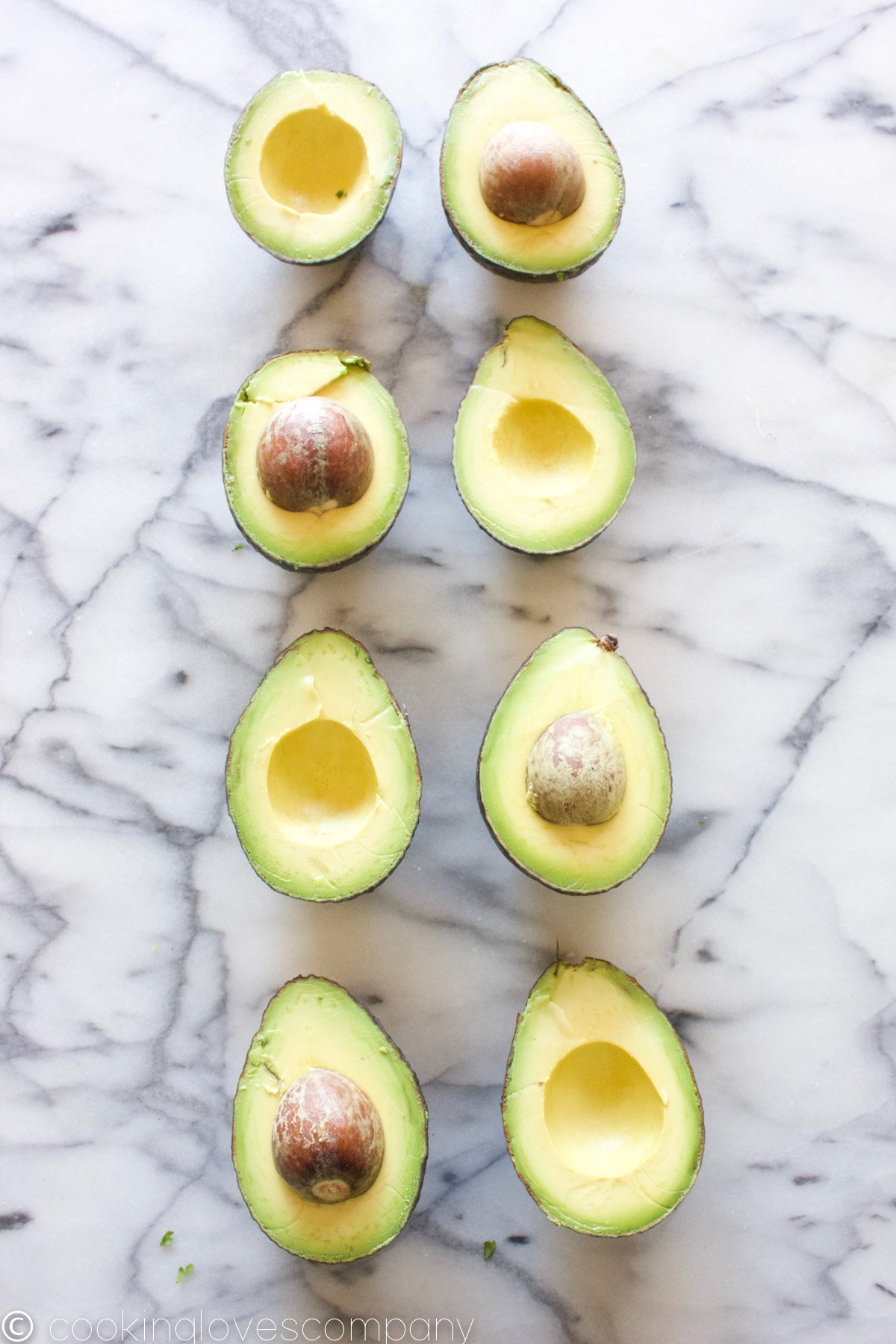 4, halved avocados in 2 vertical lines on a marble countertop 