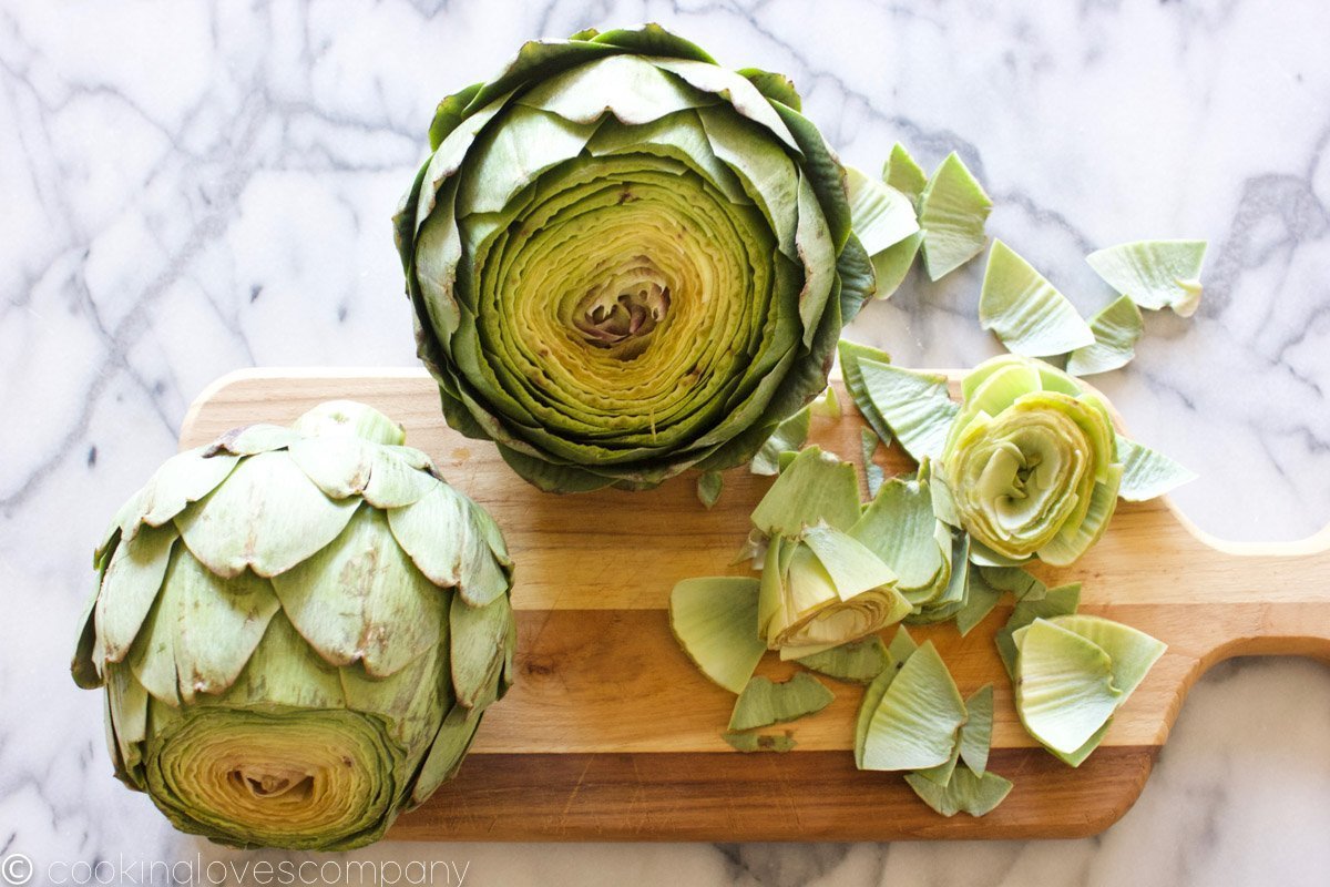 Two artichokes with the tops cut off on a cutting board