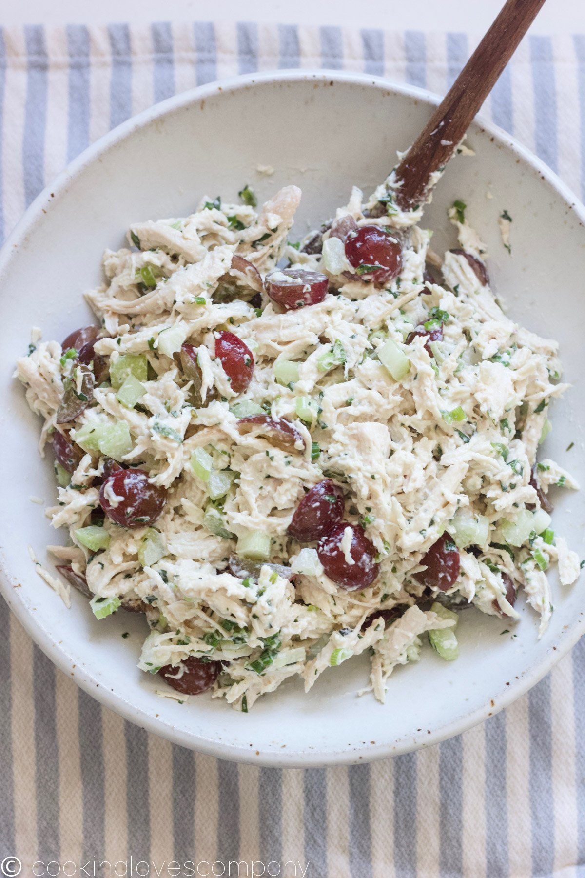 A bowl of tarragon chicken salad with celery, scallions and grapes in a bowl with a wooden spoon in it.