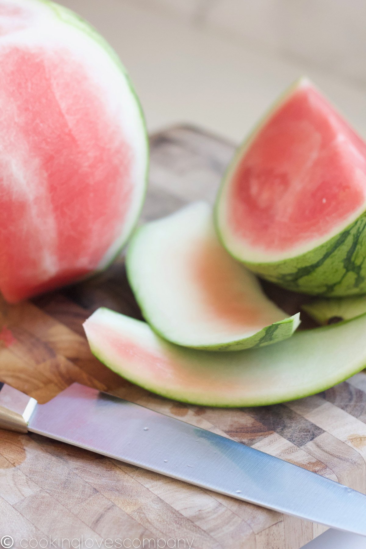 Watermelon being sliced on a cutting board with a knife in the foreground