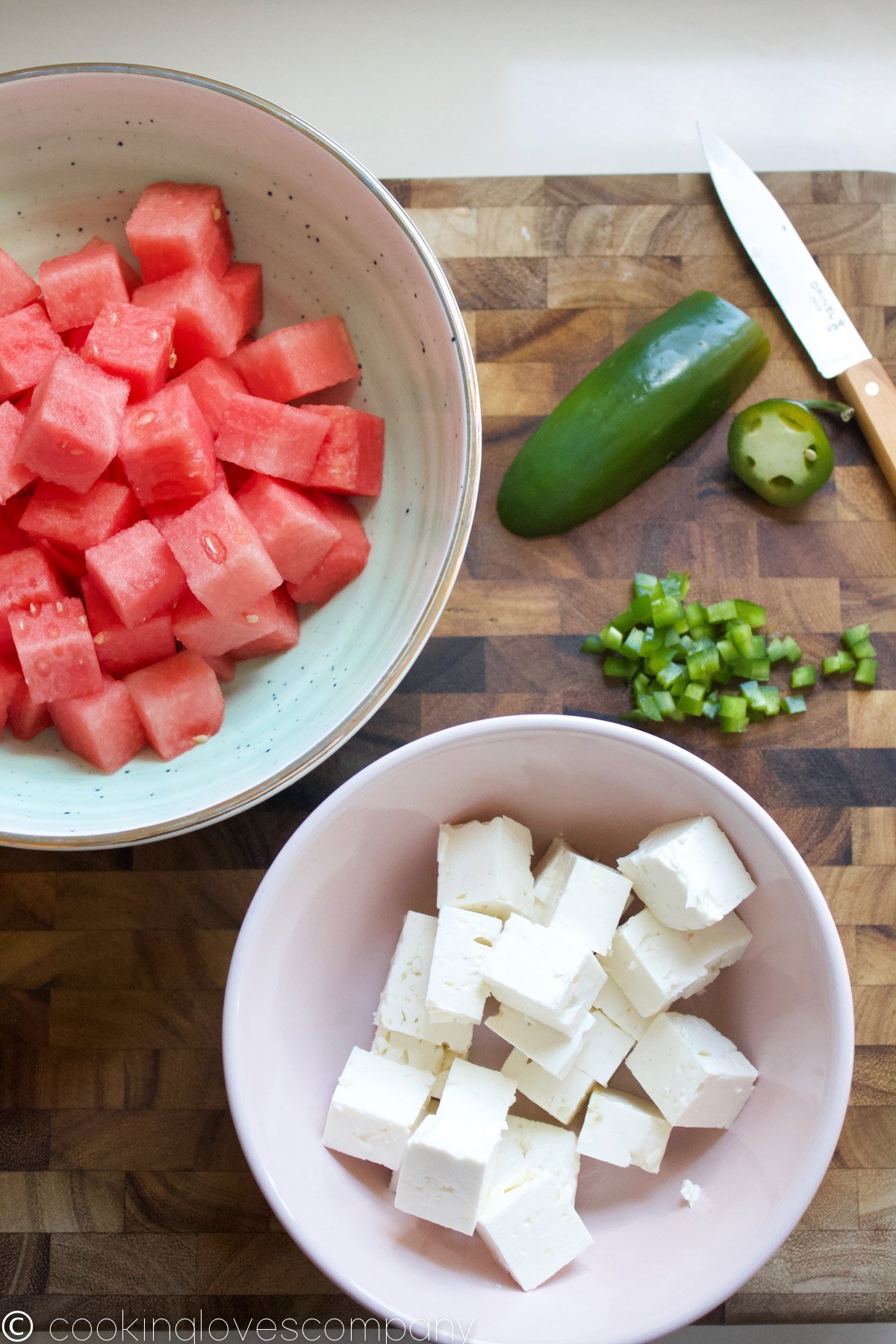 Overhead shot of cubed watermelon and feta cheese in bowls, with a diced jalapeno on a cutting board
