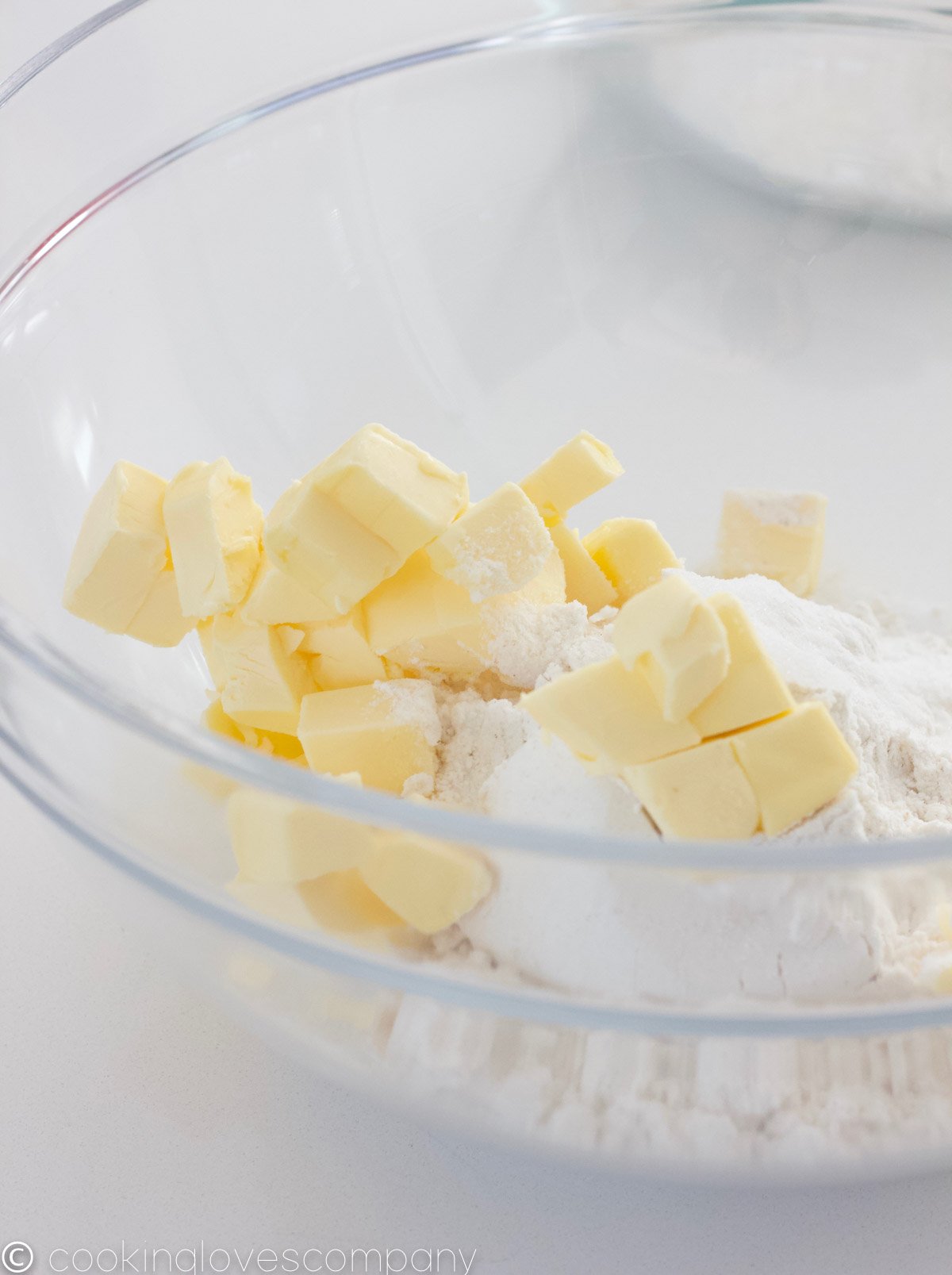 Close up of a glass mixing bowl with cubed butter, sugar and flour