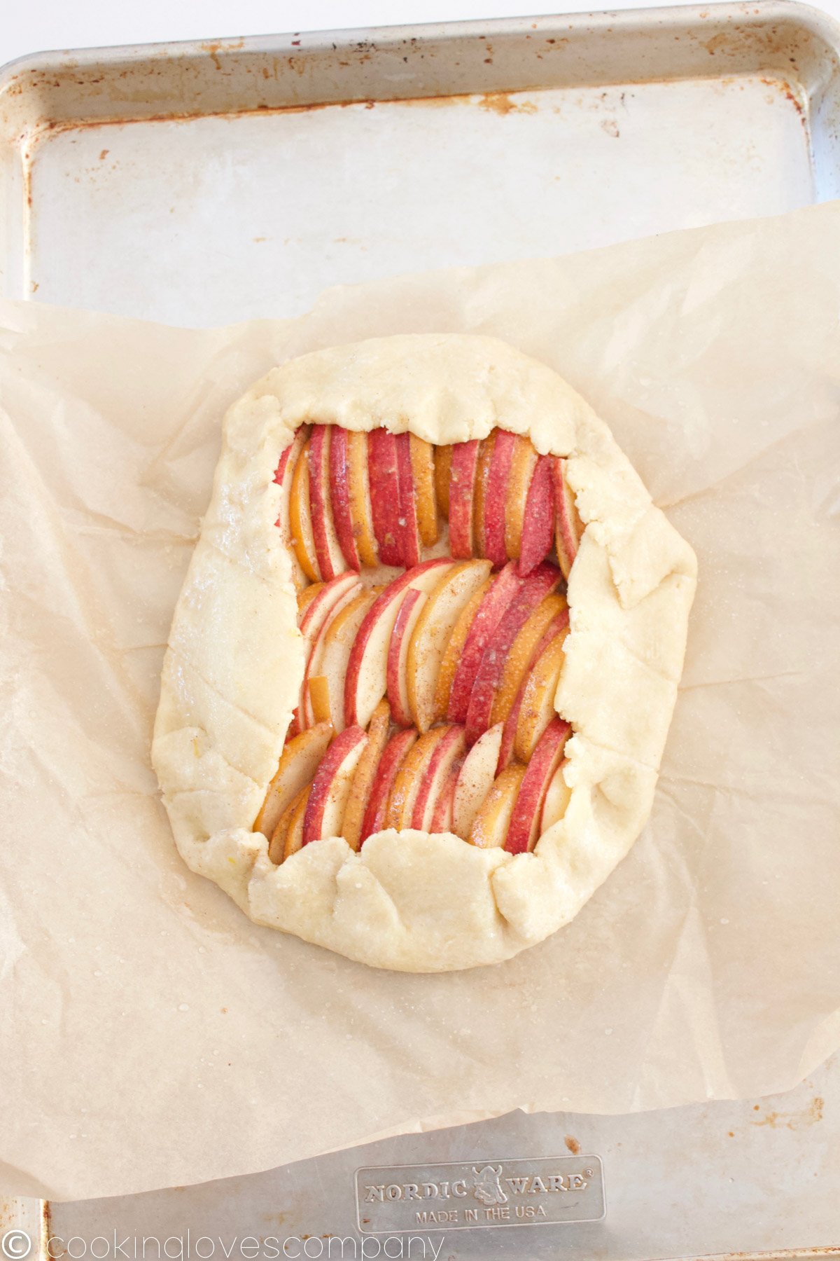 Raw apple and pear galette on a parchment lined baking sheet