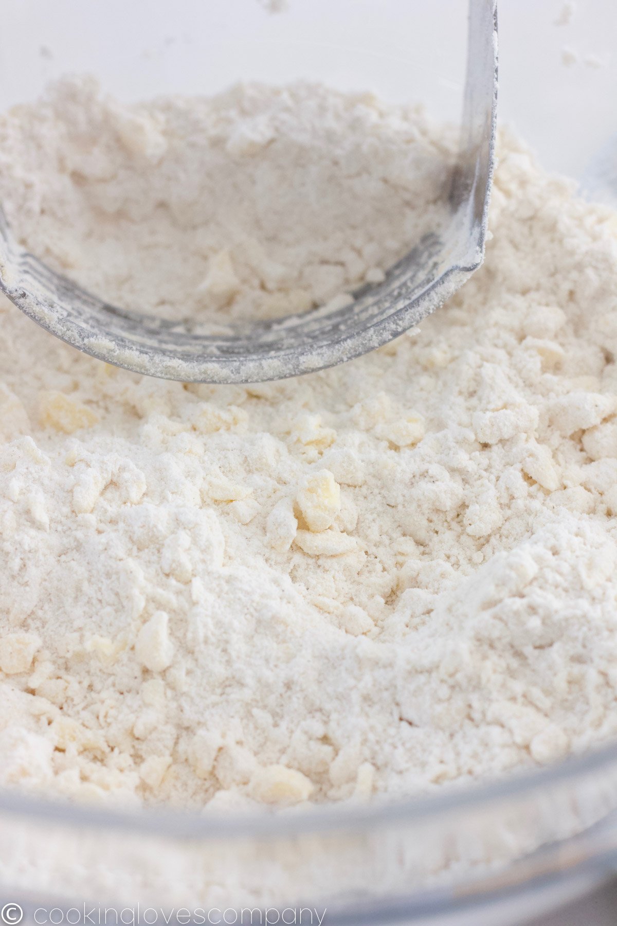 Close up of a glass mixing bowl filled with flour and bits of butter and a pastry cutter