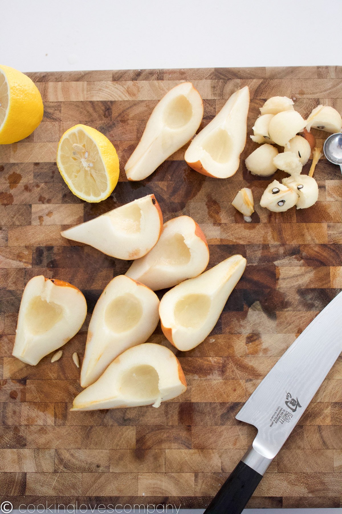 Flat lay of quartered and seeded pears on a wooden cutting board with a halved lemon and chefs knife
