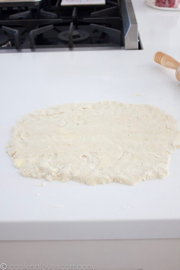 Rolled out pastry dough on a white counter with a black stove top and handle of a rolling pin in the background