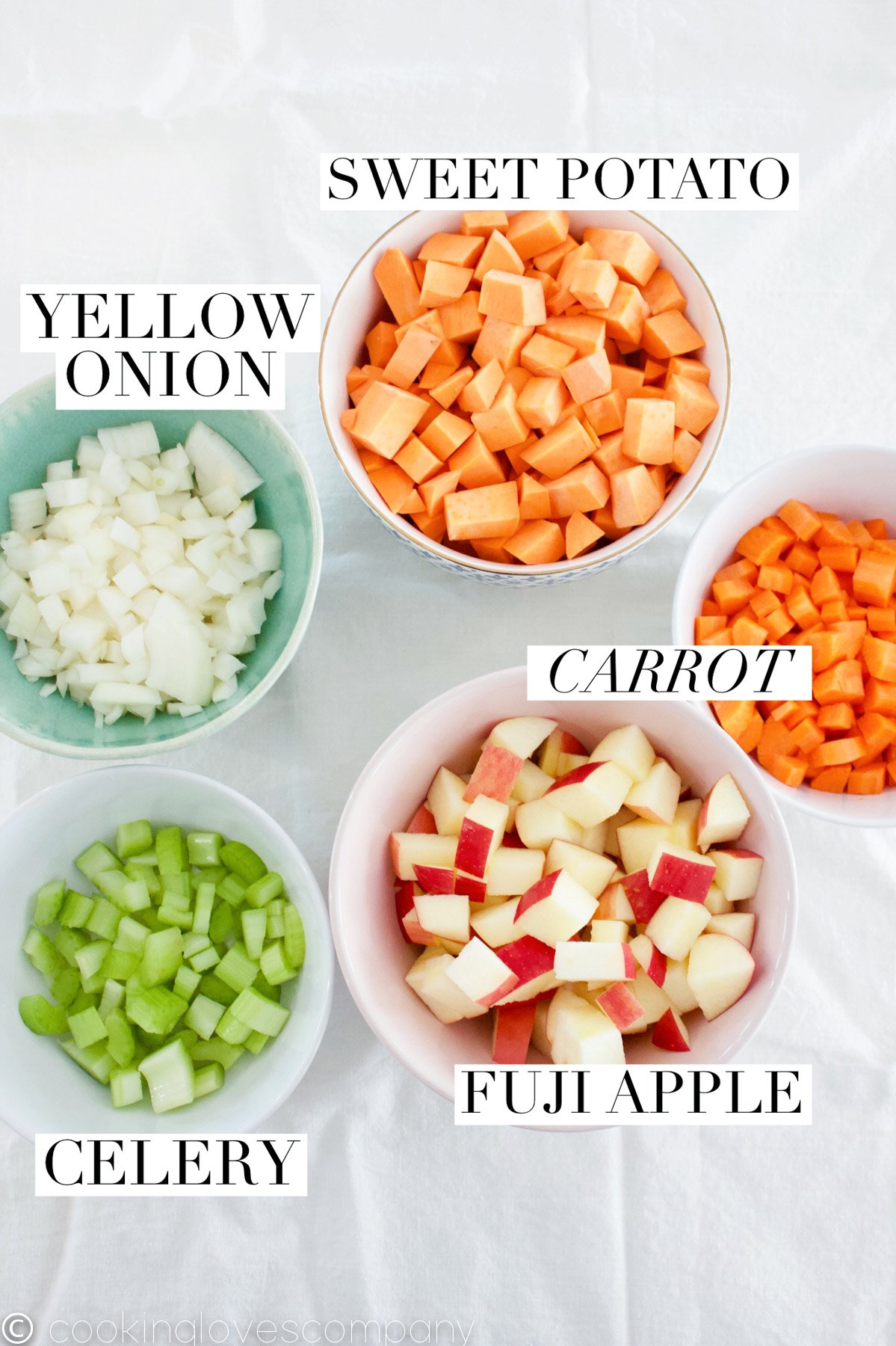 Flatlay photo of 5 bowls on a table, filled with diced carrots, sweet potatoes, onions, celery and apples.
