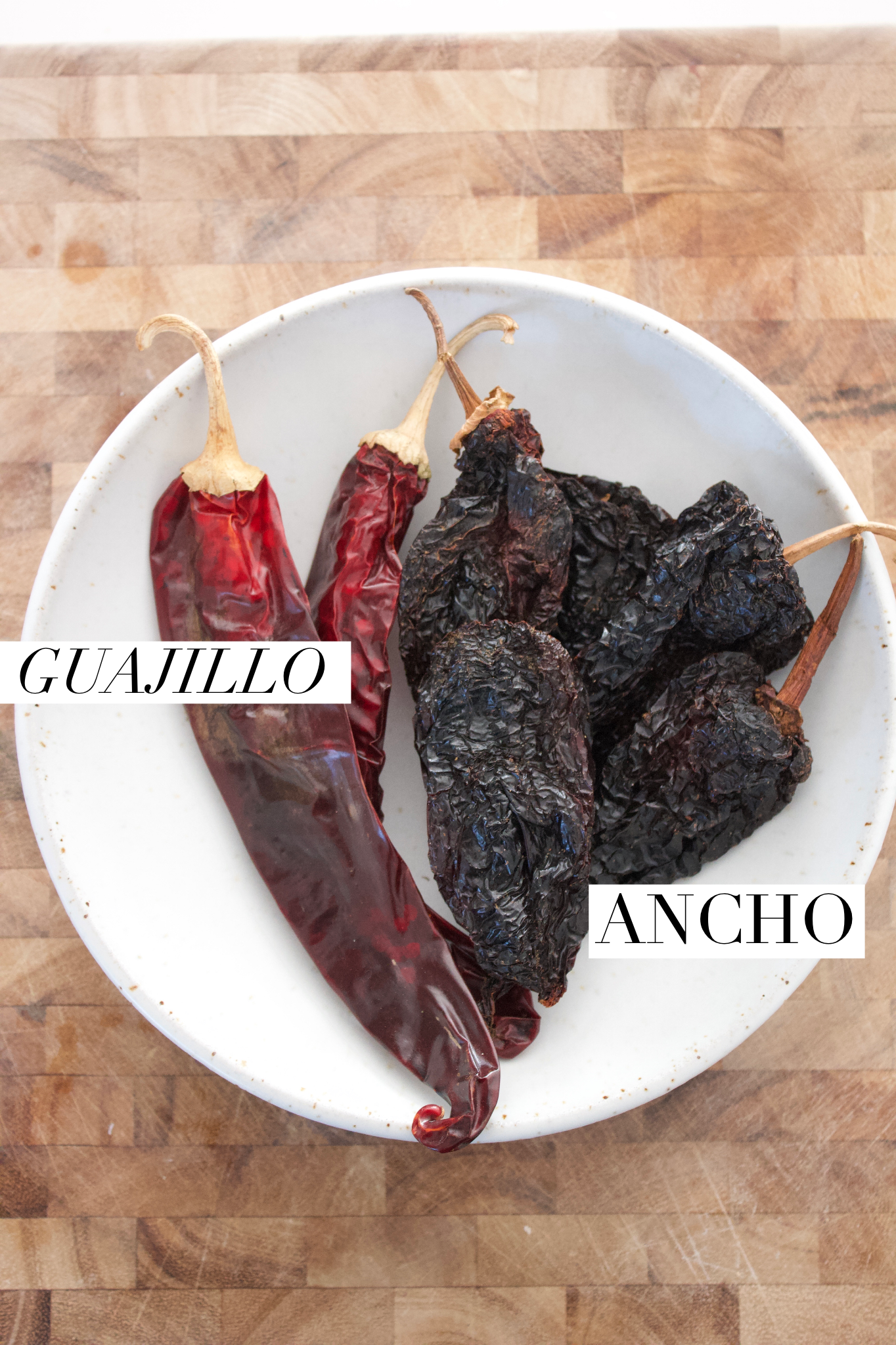 Dried guajillo and ancho chiles in a bowl on a cutting board