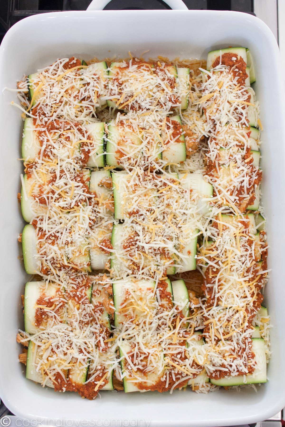 Zucchini Enchiladas with red sauce and shredded cheese in a casserole dish
