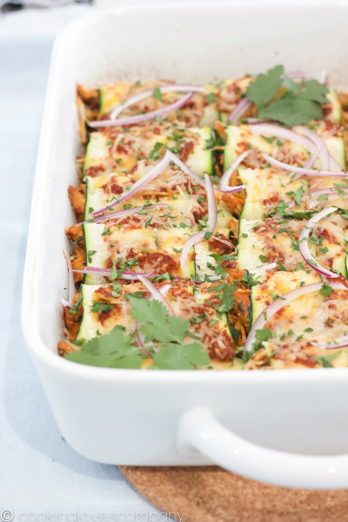 Cooked Zucchini Enchiladas in a white casserole dish on a cork trivet