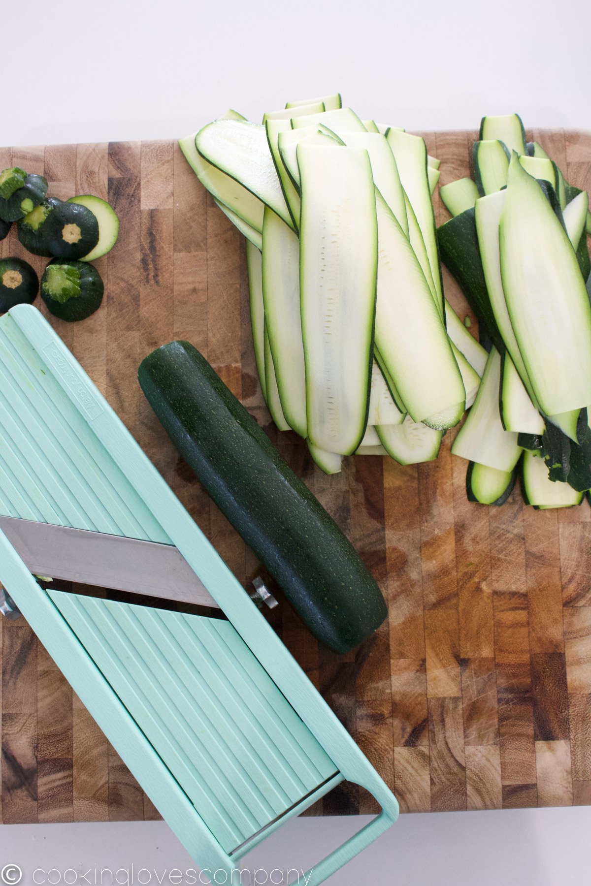 Thinly sliced zucchini on a cutting board next to a mandoline
