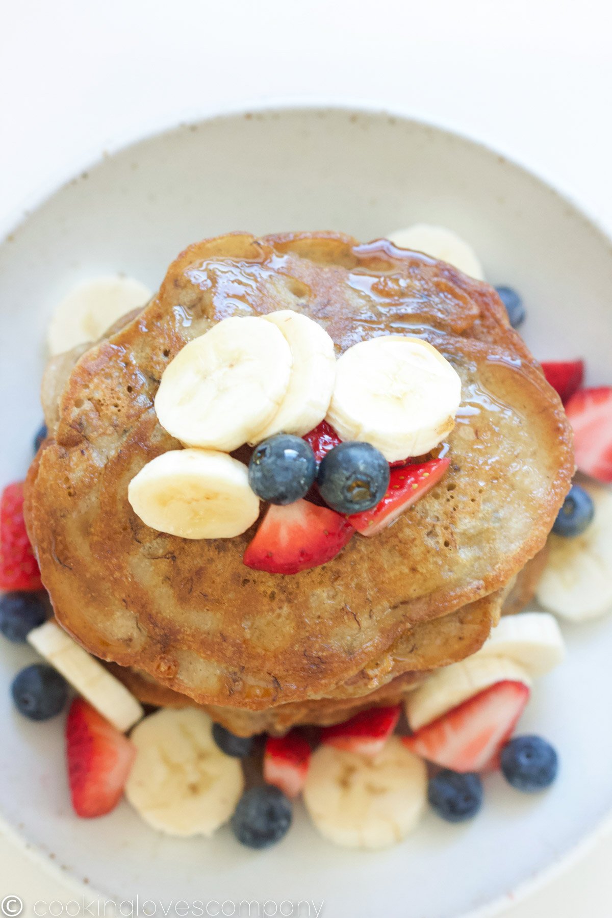 An flatlay shot of a stack of banana pancakes with fresh berries and bananas